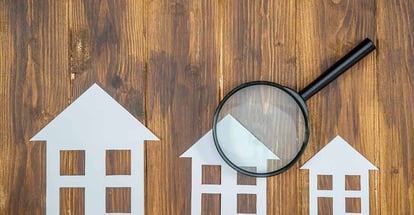 Paper house with magnifying glass on wooden table