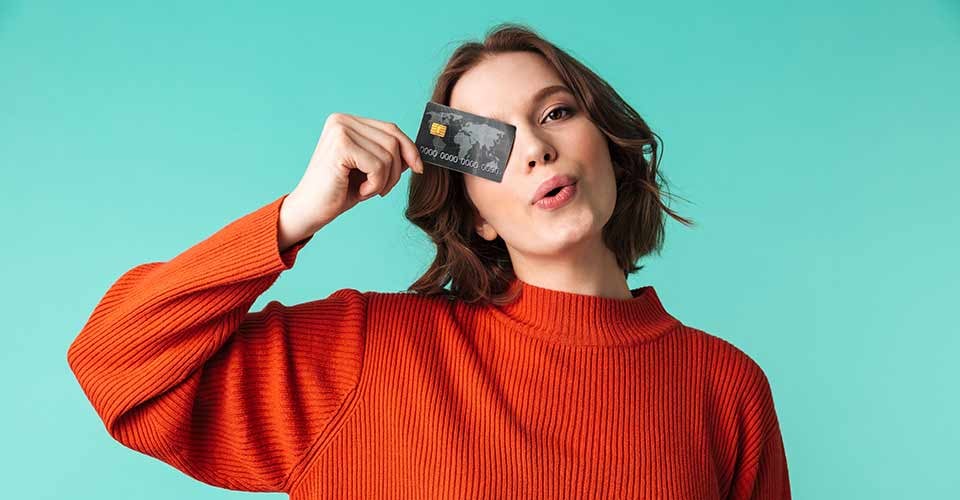 Portrait of a pretty young woman dressed in sweater holding credit card at her face
