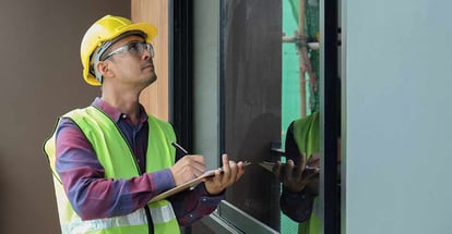 Professional inspector is checking building structure around window with checklist in hand