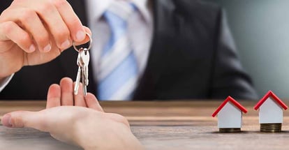 Real estate agent giving house keys to buyer and model house on coins stack