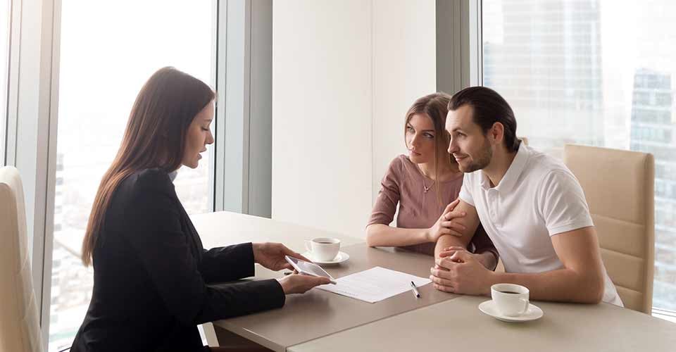 Realtor and young couple sitting at desk to discuss new house purchase