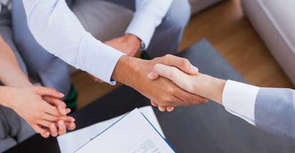 Salesman shaking hands with client with contract on the coffee table