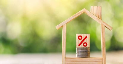 Small wooden shaped house with stack of coins and percent symbol on cube