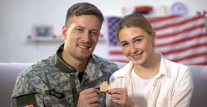 Smiling US male soldier and his wife showing wooden house sign in their new home