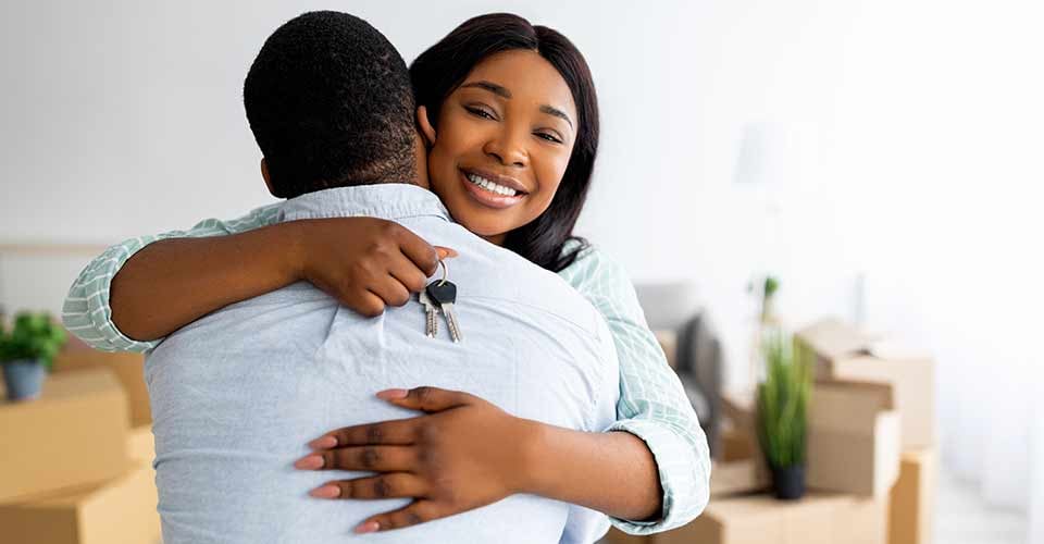 Smiling black lady holding house key and hugging her husband after moving to new home