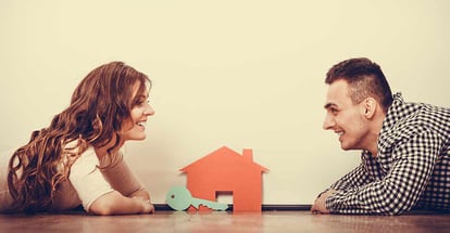 Smiling couple lying on floor with modal house and key