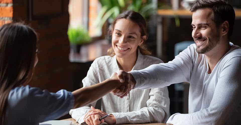Smiling couple making successful deal and handshaking with realtor