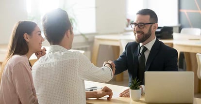 Smiling realtor handshaking young couple thanking for advice