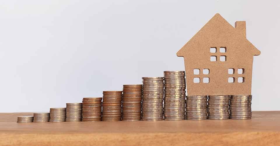 Stack of coins and house model on wooden table