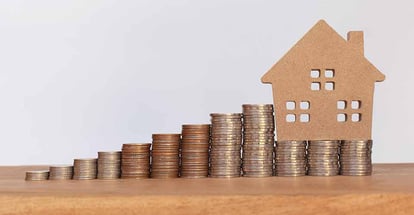Stack of coins and house model on wooden table