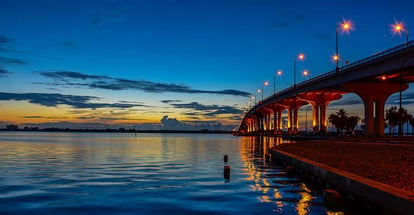 The sun coming up over the Indian River lagoon in Florida with a causeway bridge lit with street lights