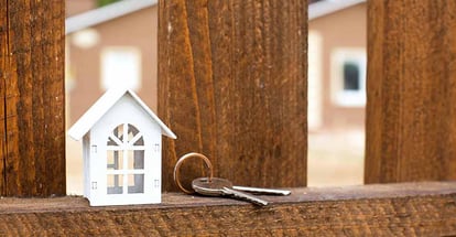 White wooden model home on fence with house key