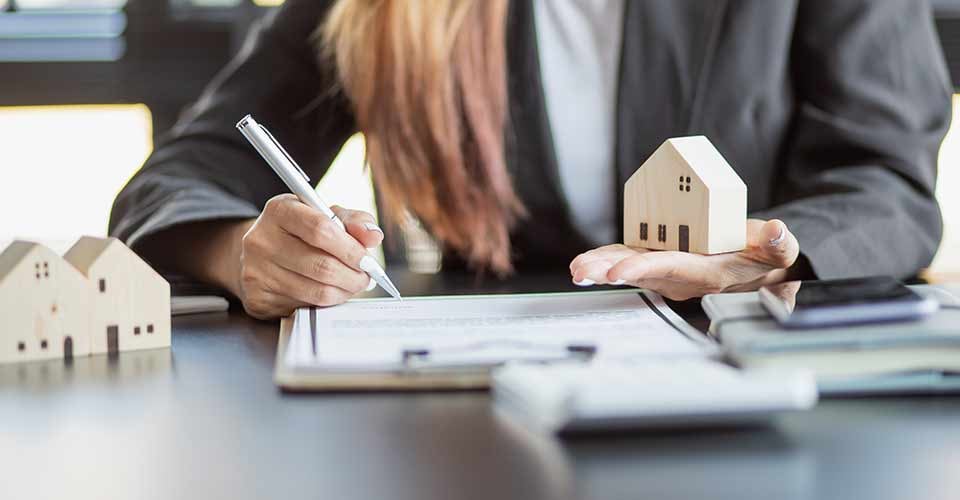 Woman hand holding model house and signing home purchase contract