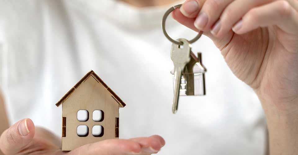 Woman holding a house key and a wooden model house