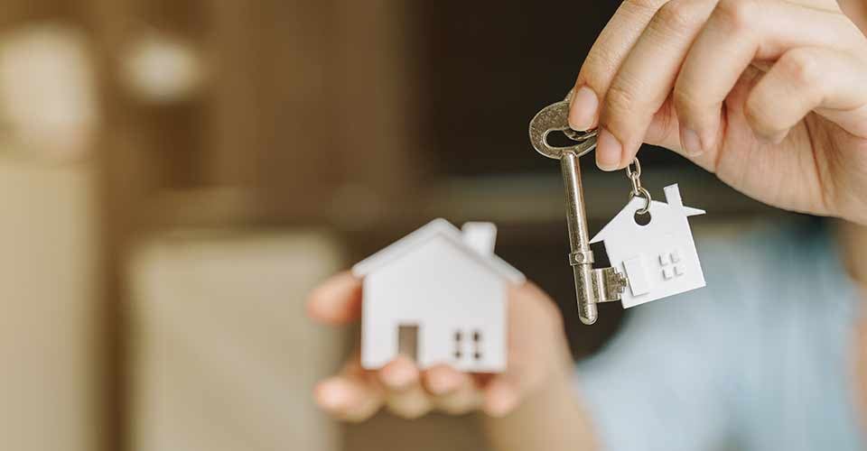Woman holding white house model and house key in hand