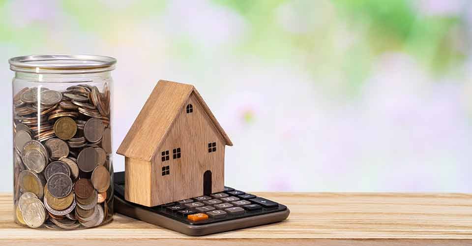 Wooden home model coins holder and calculator on wooden table for real estate investment