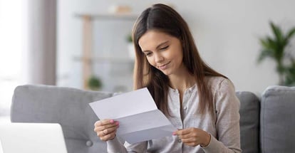 Young attractive woman sitting on sofa at home reading loan approval paper