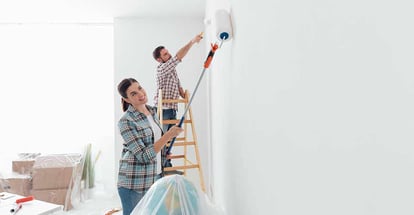 Young happy couple painting their new house interiors using paint rollers
