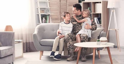 Young man in military uniform with his children on sofa at home