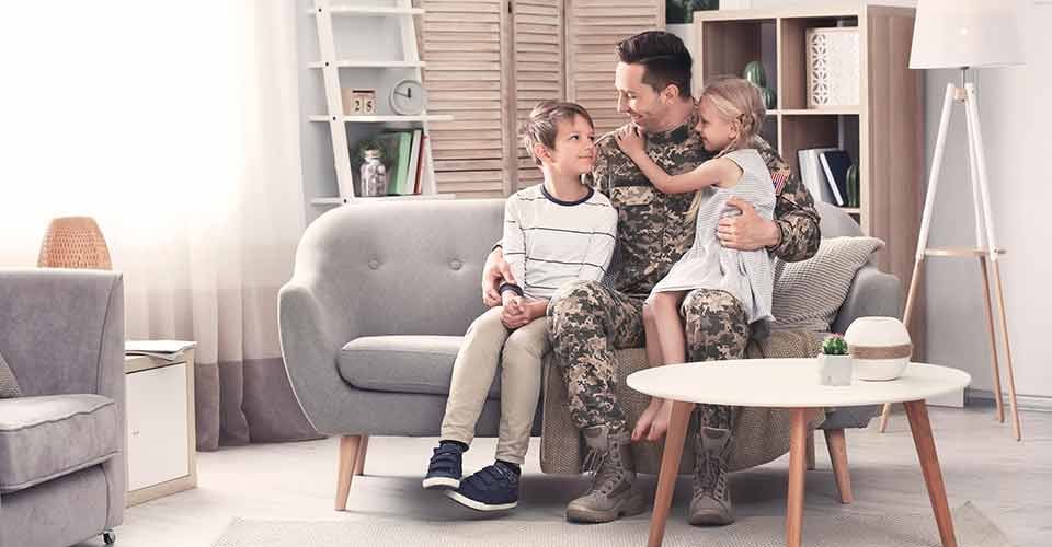 Young man in military uniform with his children on sofa at home