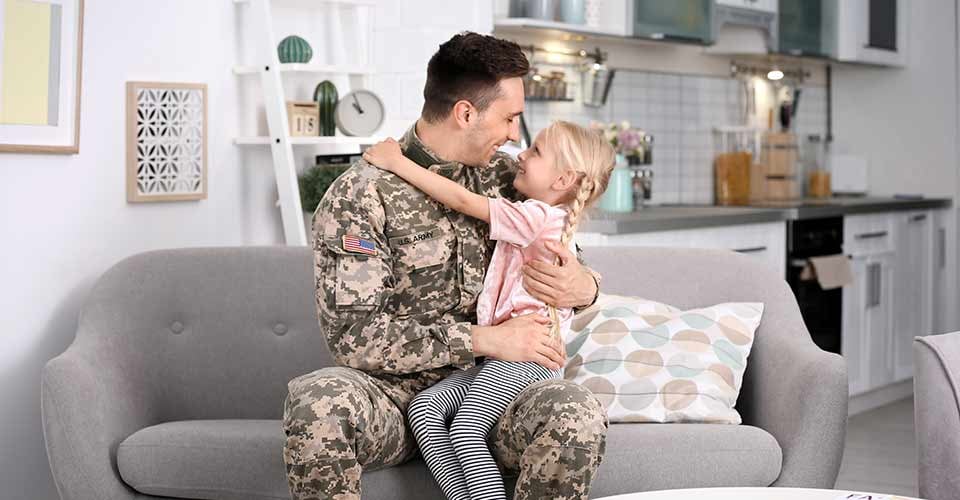 Young man in military uniform with his little daughter on sofa at home