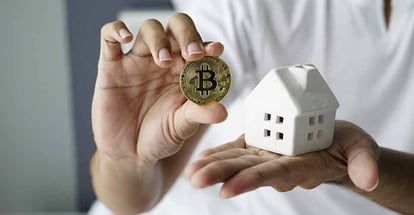 Young person holding bitcoin and model home in hand