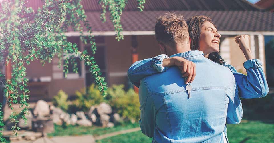 Young smiling couple showing keys to new home hugging