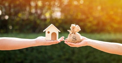 A man and a women hand holding a money bag and a model home