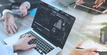 Business documents on office table with laptop graph and three colleagues discussing data