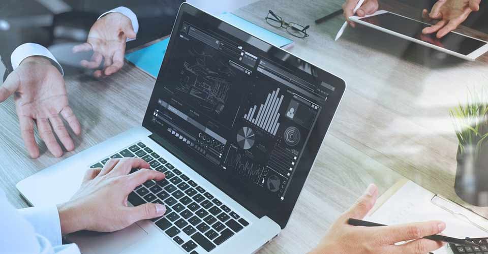 Business documents on office table with laptop graph and three colleagues discussing data