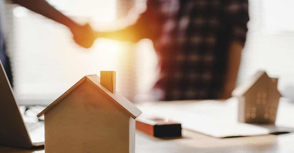 Wooden house model on workplace desk with construction worker shaking hands