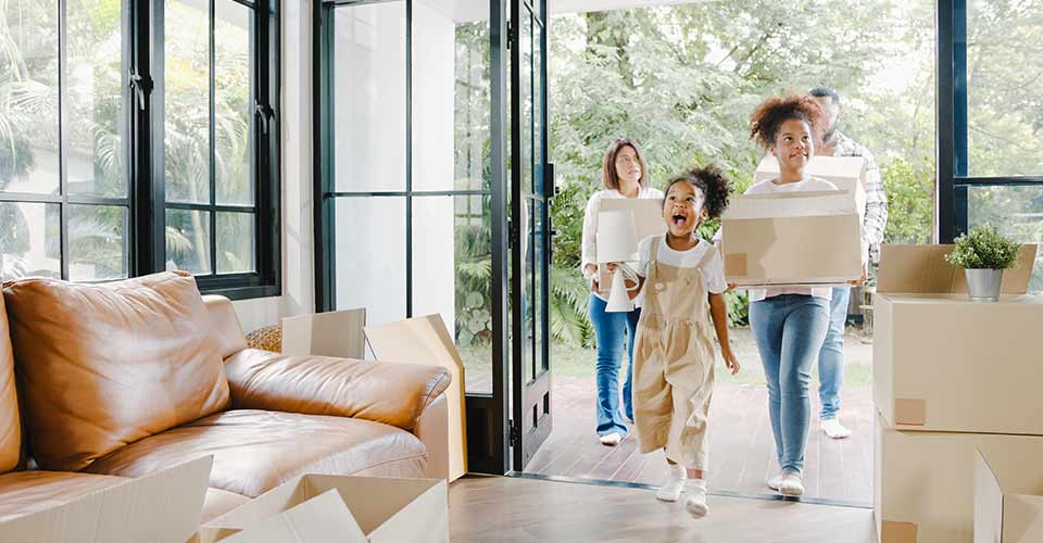 Happy African American family holding cardboard boxes and walking into big modern home