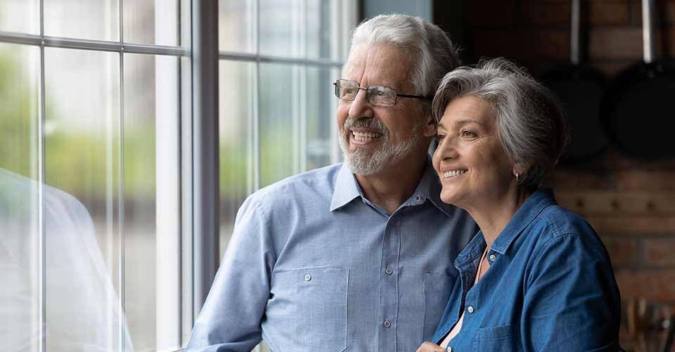 Happy middle aged senior retired couple standing near window