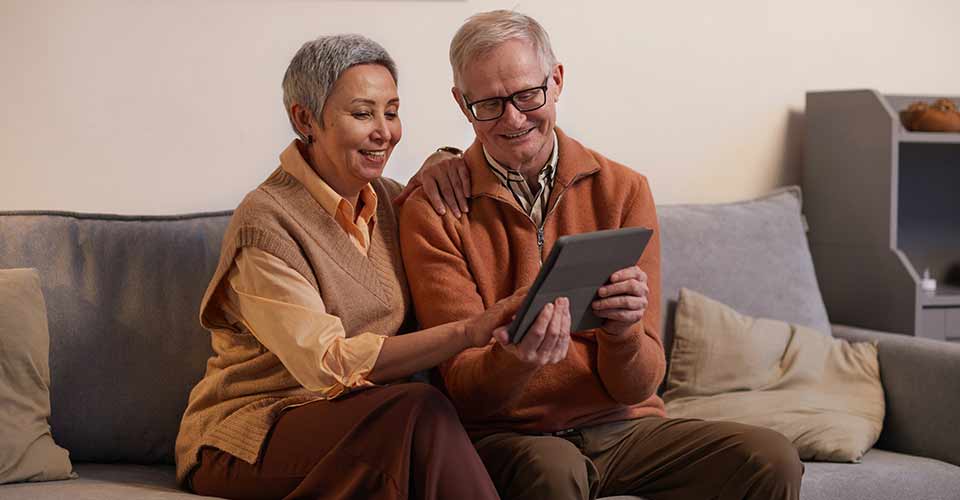Man and Woman Sitting on Sofa While Looking at a Tablet